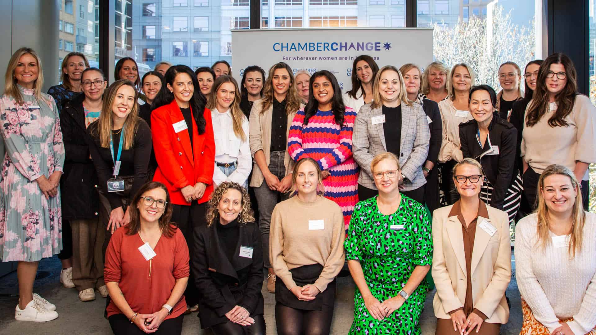A group of women all smile and sit for the camera at an event. They are all in bright clothes.