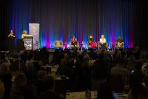 A panel presentation at a conference, with four people on the panel and a moderator behind a lectern. The image is from the DEA Conference 2024. It is a wide angle shot so we can't see the people in detail.