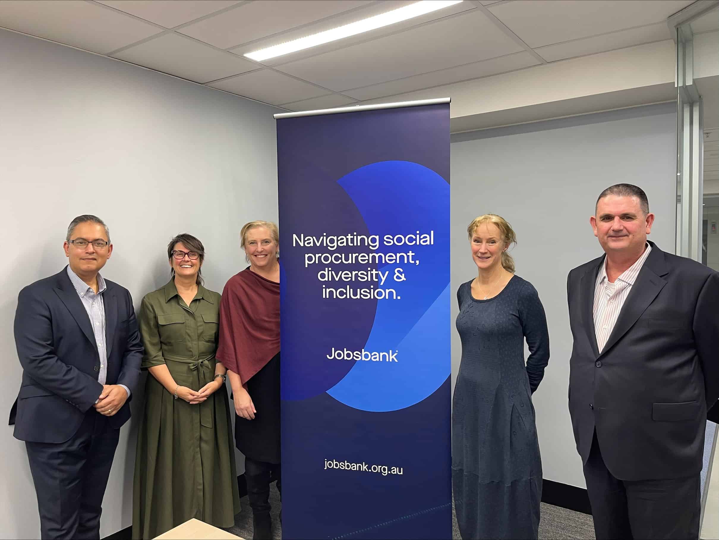 Five people, all dressed in professional clothes, stand in front of a Jobsbank banner. There are three women and two men.