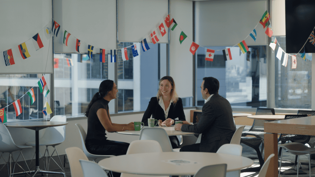 A group of three people sitting at a round table with various different country's flags hanging above them.