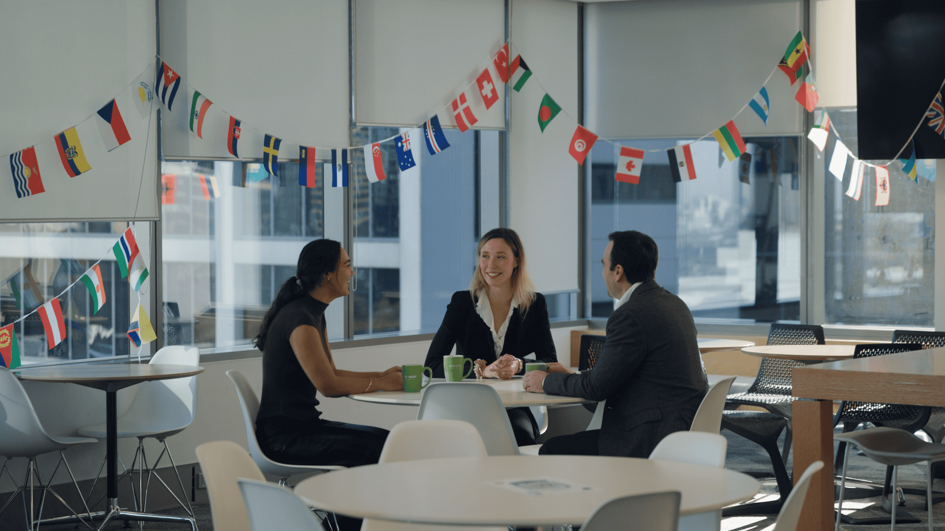 A group of three people sitting at a round table with various different country's flags hanging above them.