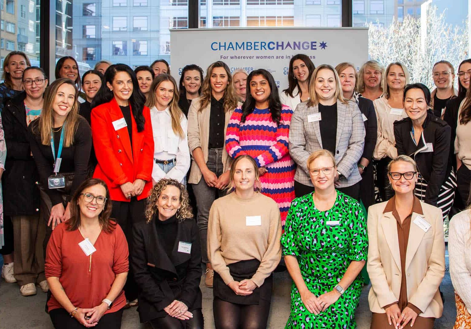 A group of women all smile and sit for the camera at an event. They are all in bright clothes.
