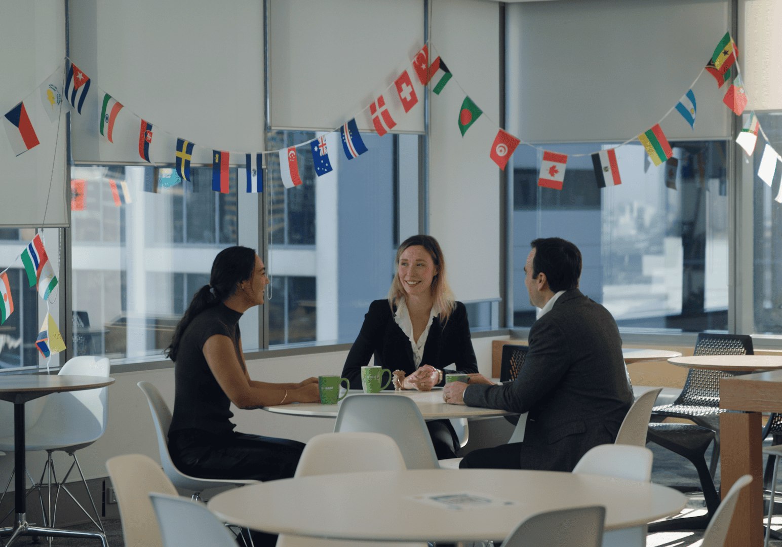 A group of three people sitting at a round table with various different country's flags hanging above them.
