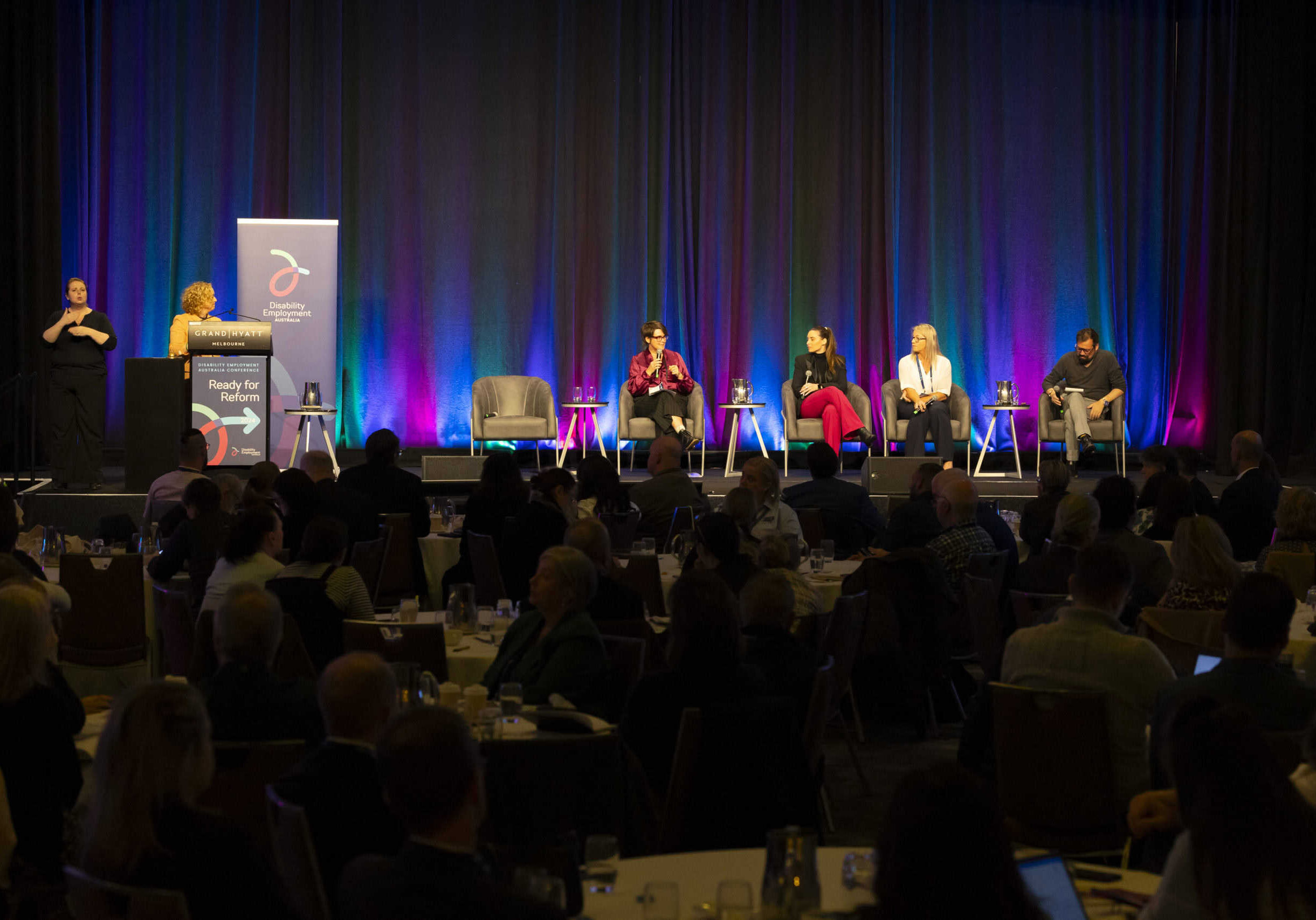 A panel presentation at a conference, with four people on the panel and a moderator behind a lectern. The image is from the DEA Conference 2024. It is a wide angle shot so we can't see the people in detail.