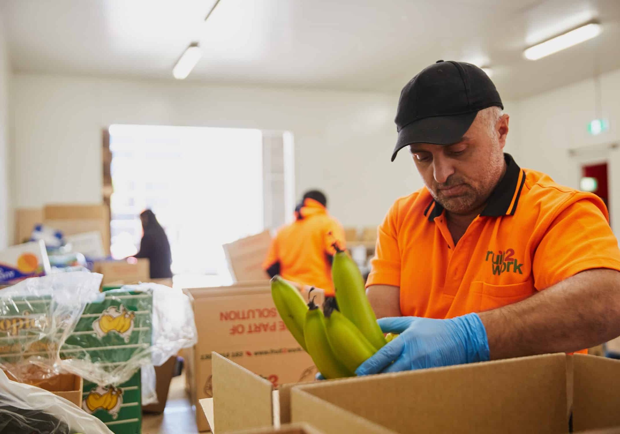 A man wearing high-visibility workwear packs fruit in a cardboard box