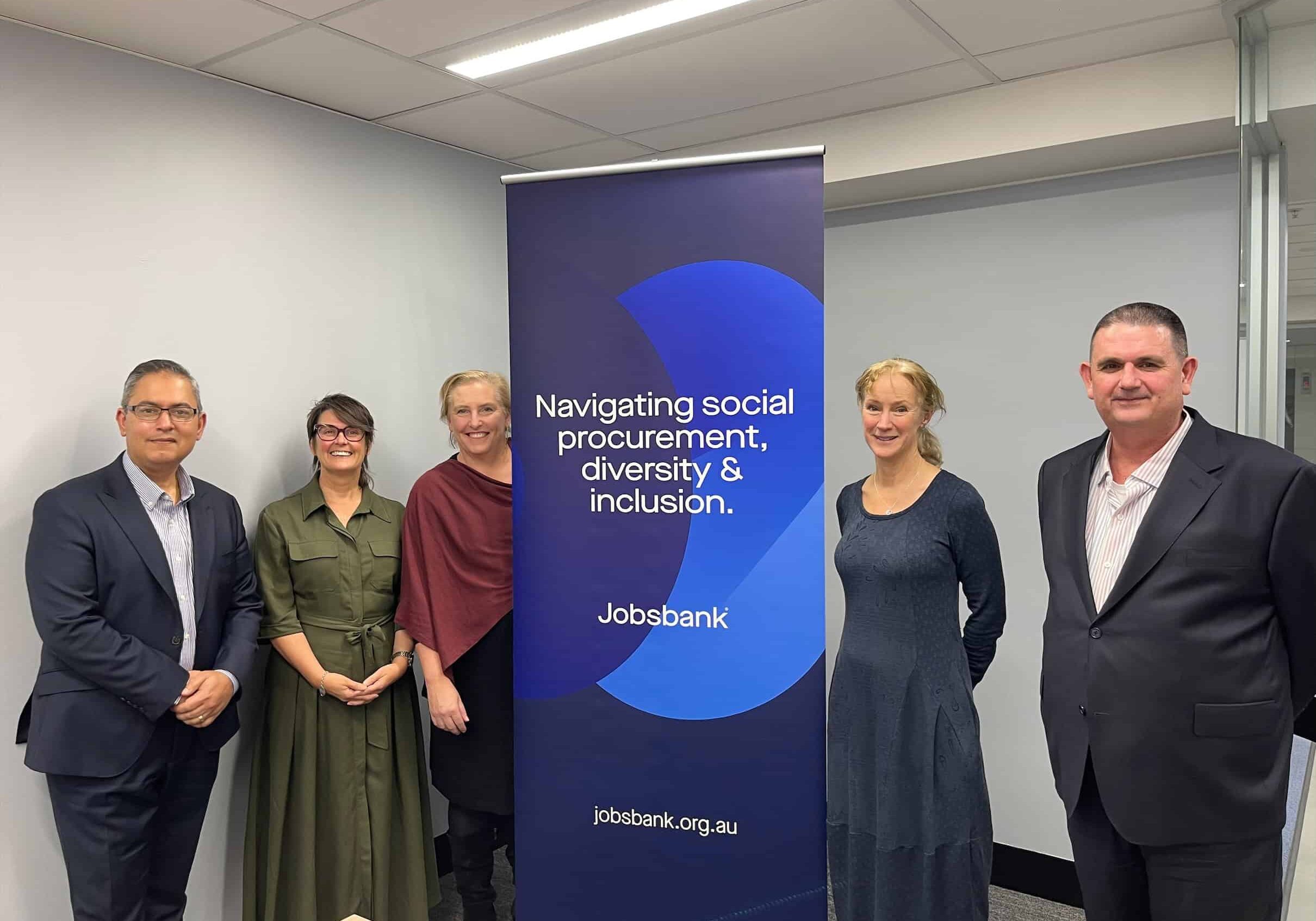 Five people, all dressed in professional clothes, stand in front of a Jobsbank banner. There are three women and two men.